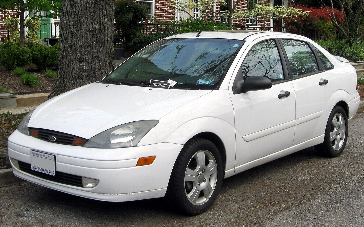 Front three-quarter view of a white four-door compact saloon of early 2000s design, wearing a Washington, D.C. licence plate, parked on a residential street.