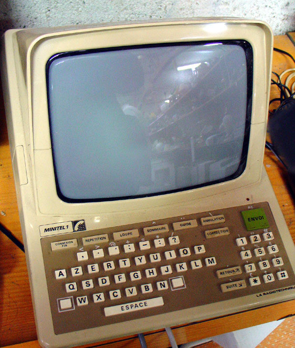 A beige early-1980s videotex terminal with a built-in monochrome screen and a fold-down AZERTY keyboard, standing on a wooden table.