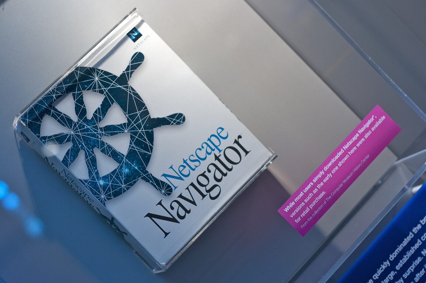 A shrink-wrapped Netscape Navigator software box, white with a dark blue ship's-wheel logo, propped in a glass museum case beside a pink explanatory label.