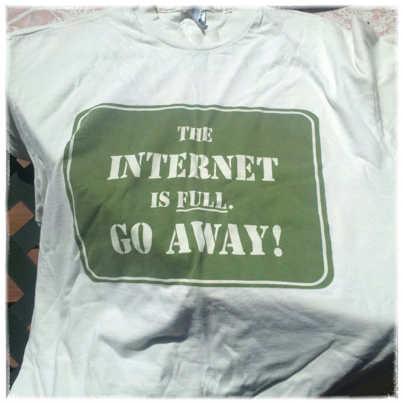 A white T-shirt printed with a green-bordered panel reading “The Internet is full. Go away!” in stencilled capitals.