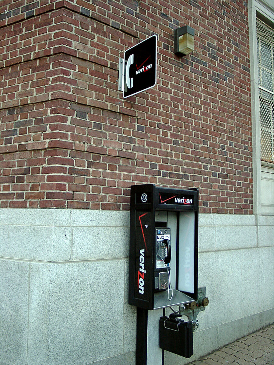 A street payphone in its enclosure beside a pavement, photographed from the footway.