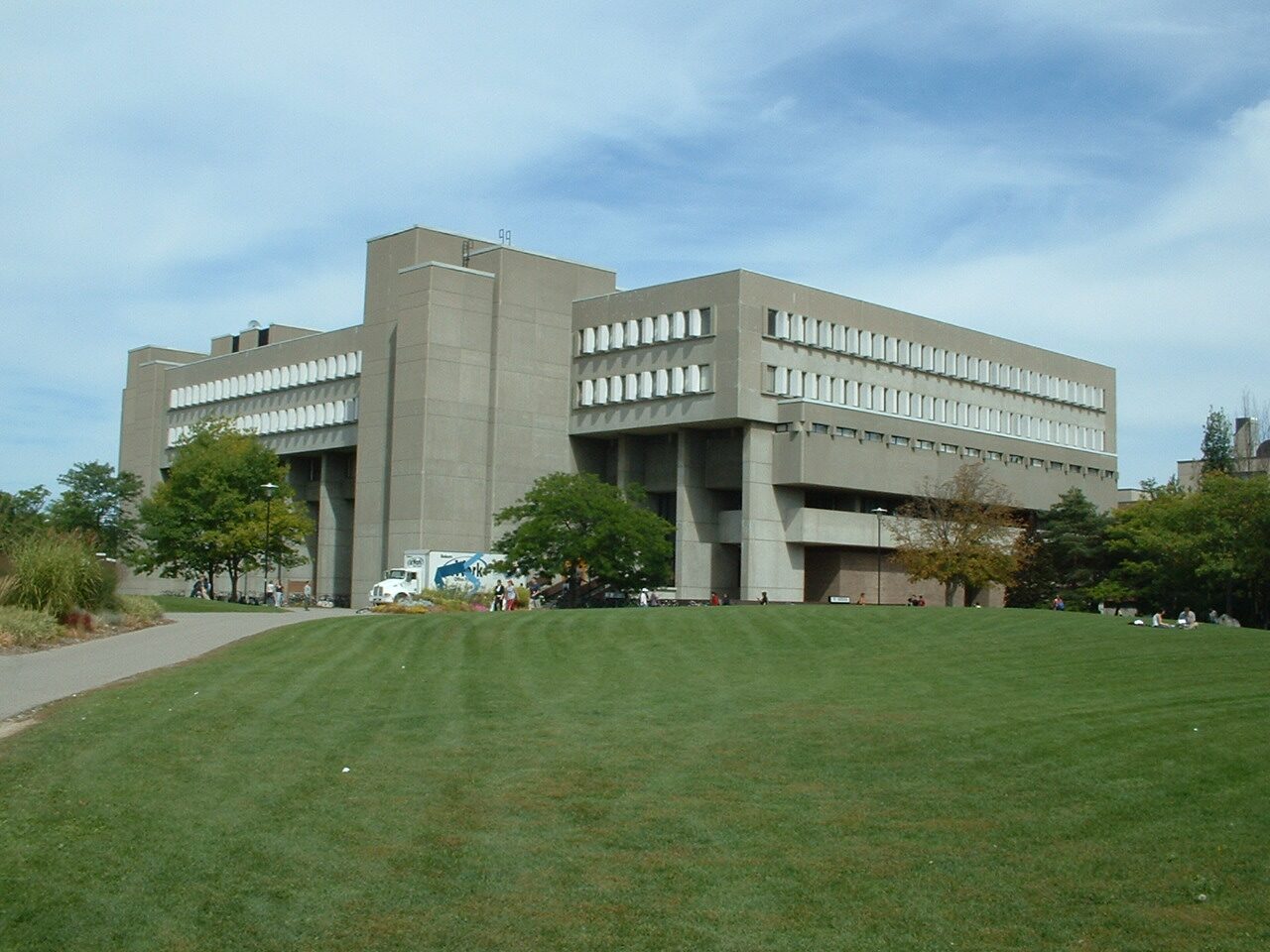 A large concrete university building with rows of windows, seen from outside across a lawn.