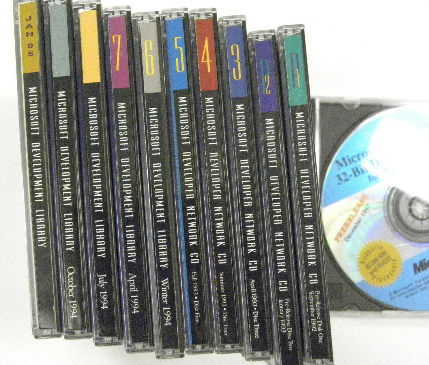 Ten CD jewel cases stood on edge in a row, spines reading Microsoft Development Library and Microsoft Developer Network CD with dates from 1992 to 1995, beside an open case holding a disc.
