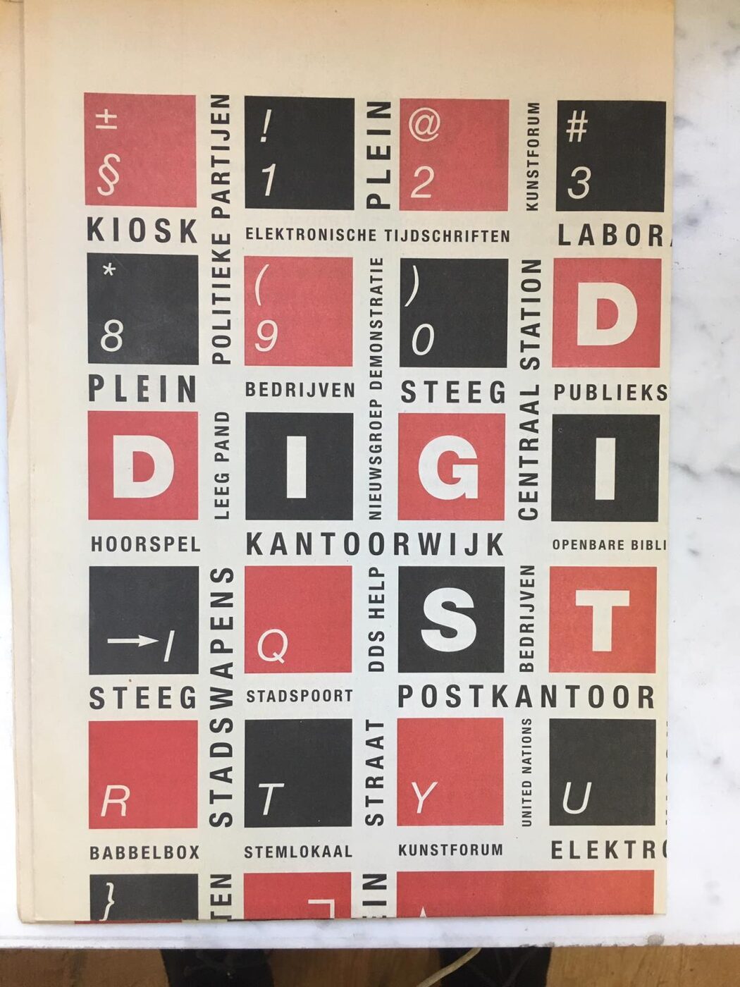 Printed cover of a Dutch tabloid newspaper: a grid of red and black squares carrying single letters and punctuation marks, captioned with words such as KIOSK, PLEIN, STEEG and POSTKANTOOR.