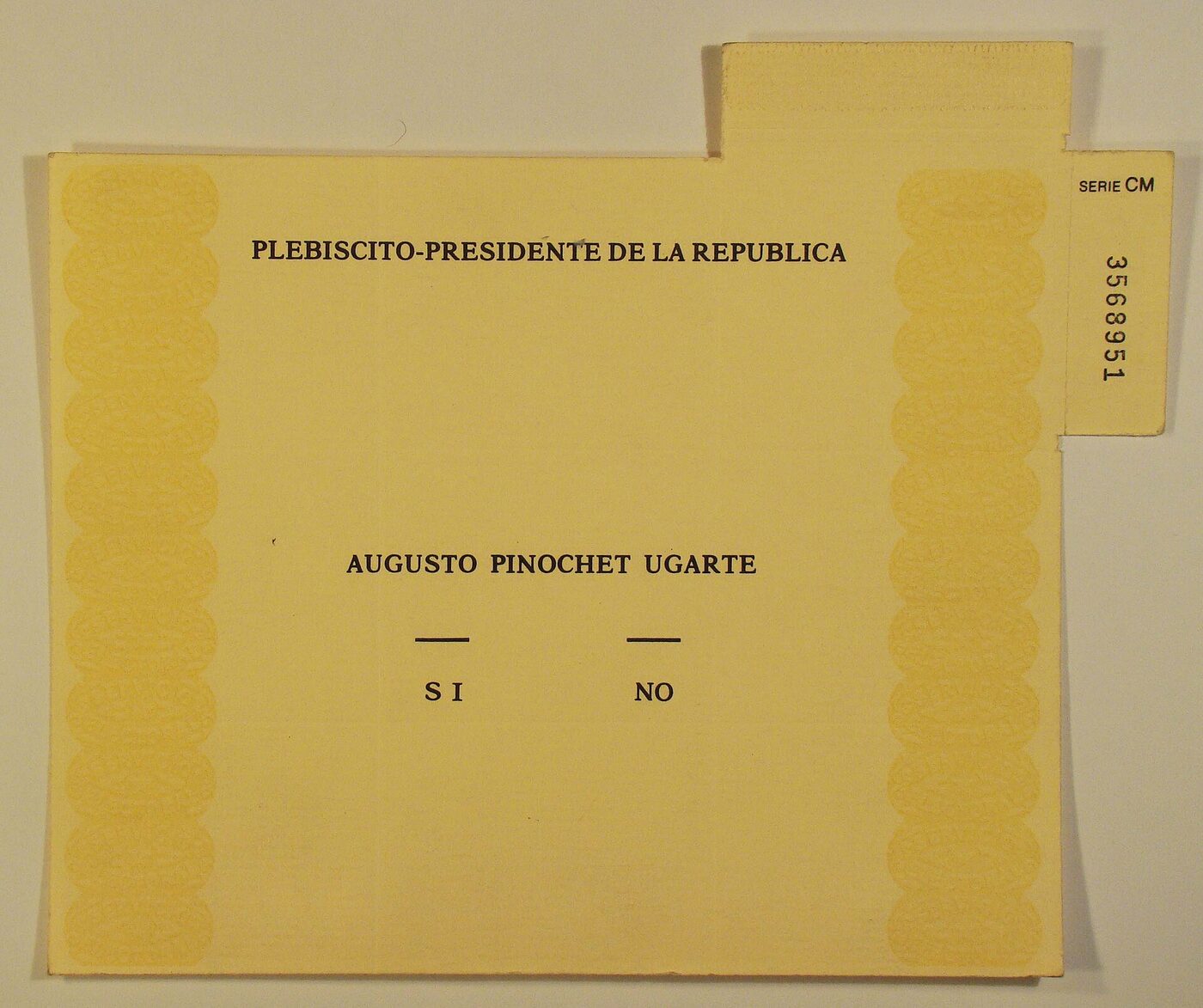 A yellow printed ballot paper headed PLEBISCITO-PRESIDENTE DE LA REPUBLICA, with the name AUGUSTO PINOCHET UGARTE above two short rules labelled SI and NO, and a numbered counterfoil at the upper right marked SERIE CM.