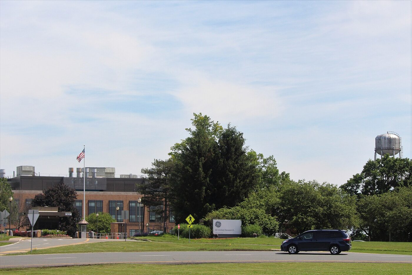 A low brick laboratory building behind trees and a lawn, with a roadside sign reading GE Global Research and a water tower to the right.
