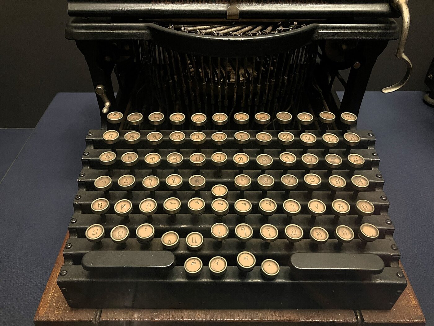 The keyboard of an antique typewriter, its keys engraved with Thai consonants, vowels and tone marks, photographed in a museum exhibition.